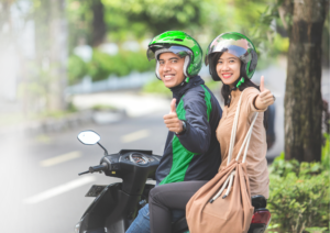 Ilustrasi pengemudi ojek online menggunakan aplikasi digital dengan latar aktivitas UMKM sebagai simbol perubahan status pengemudi menjadi pelaku usaha mikro.