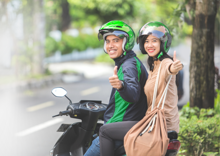 Ilustrasi pengemudi ojek online menggunakan aplikasi digital dengan latar aktivitas UMKM sebagai simbol perubahan status pengemudi menjadi pelaku usaha mikro.