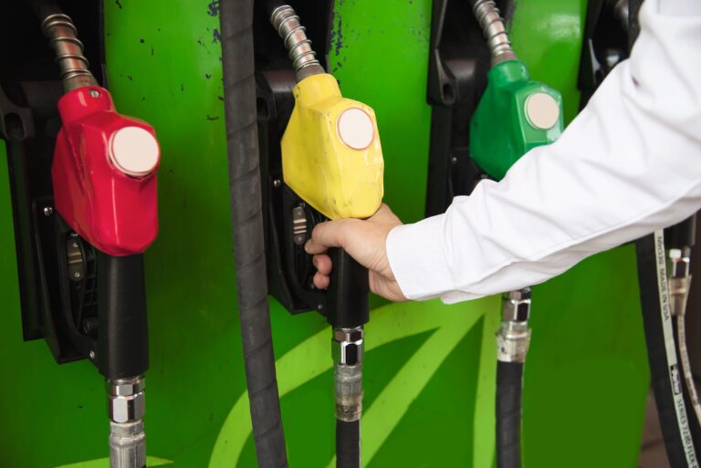 Ilustrasi truk pengangkut biodiesel B50 dengan latar fasilitas penyimpanan bahan bakar dan perkebunan kelapa sawit di Indonesia.
